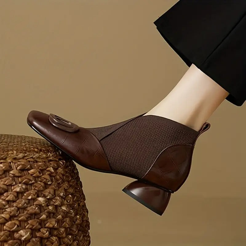 Side view of a brown ankle boot with knit panel, square toe and rounded heel, worn with black trousers 1