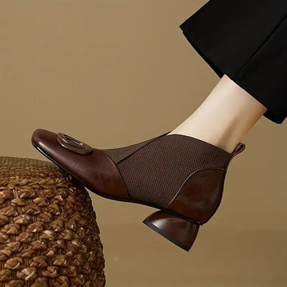 Side view of a brown ankle boot with knit panel, square toe and rounded heel, worn with black trousers 1