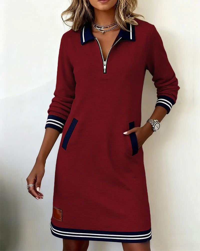 Model wearing the burgundy version with a hand in the pocket, showing the front zip, navy collar and striped trim. 5