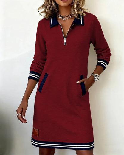 Model wearing the burgundy version with a hand in the pocket, showing the front zip, navy collar and striped trim. 5