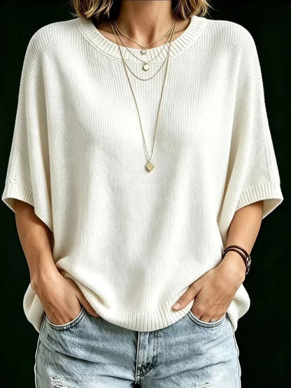 Front view of the cream knit top worn with ripped light jeans, hands in pockets and layered gold necklaces. 23