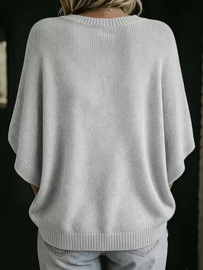 Back view of the light grey knit top on a model, showing the ribbed round neckline, wide sleeves and hem. 3