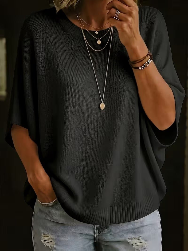 Close-up front view of the black knit top on a model with layered necklaces and one hand raised to her chin. 26