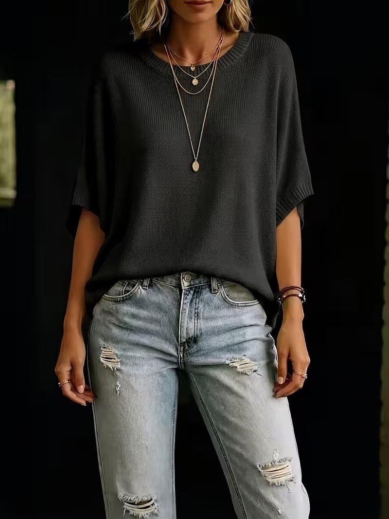 Black knit batwing top worn with distressed light-wash jeans, arms relaxed, with layered gold necklaces. 27