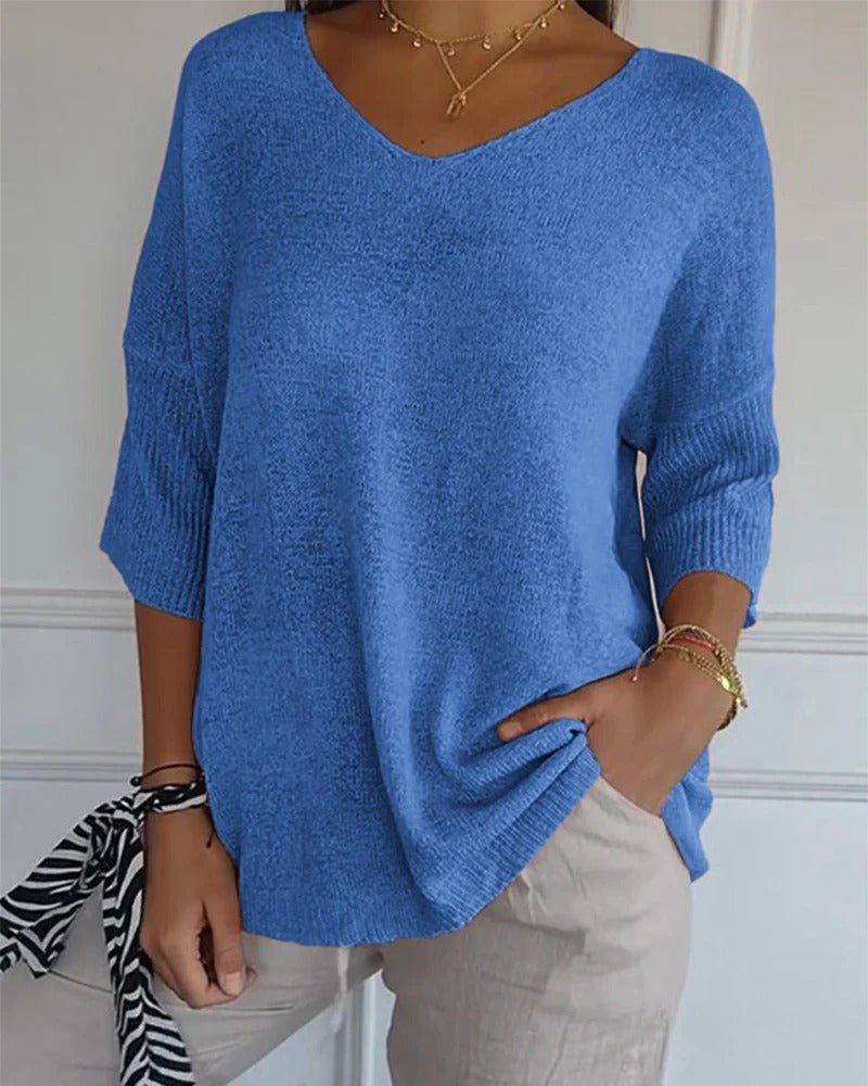 Model wearing a blue knit jumper with ribbed cuffs, styled with beige trousers and gold necklaces 1