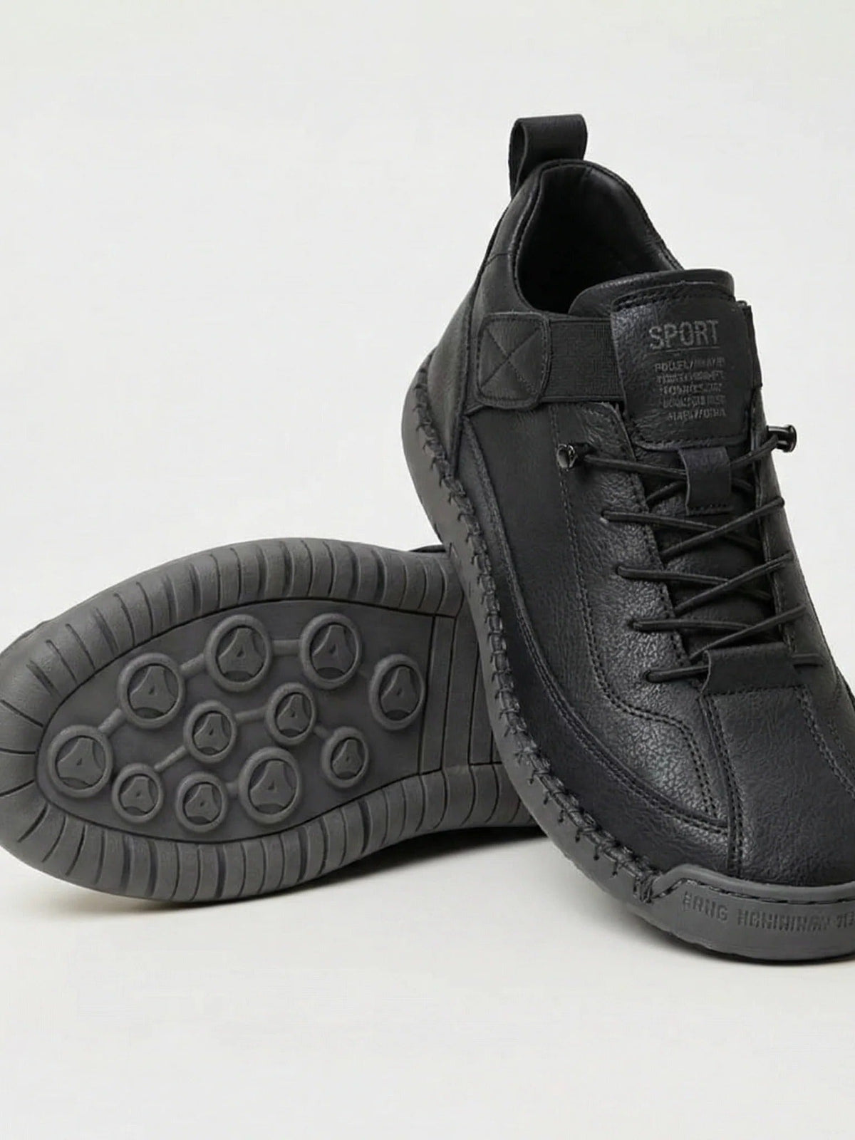 Pair of black slip-on trainers, one resting on its side to show the grey studded rubber sole 1
