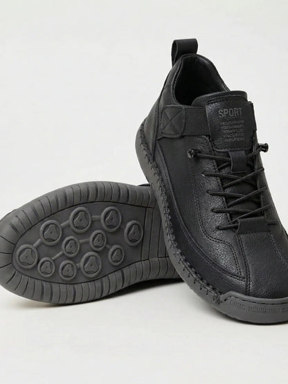 Pair of black slip-on trainers, one resting on its side to show the grey studded rubber sole 1