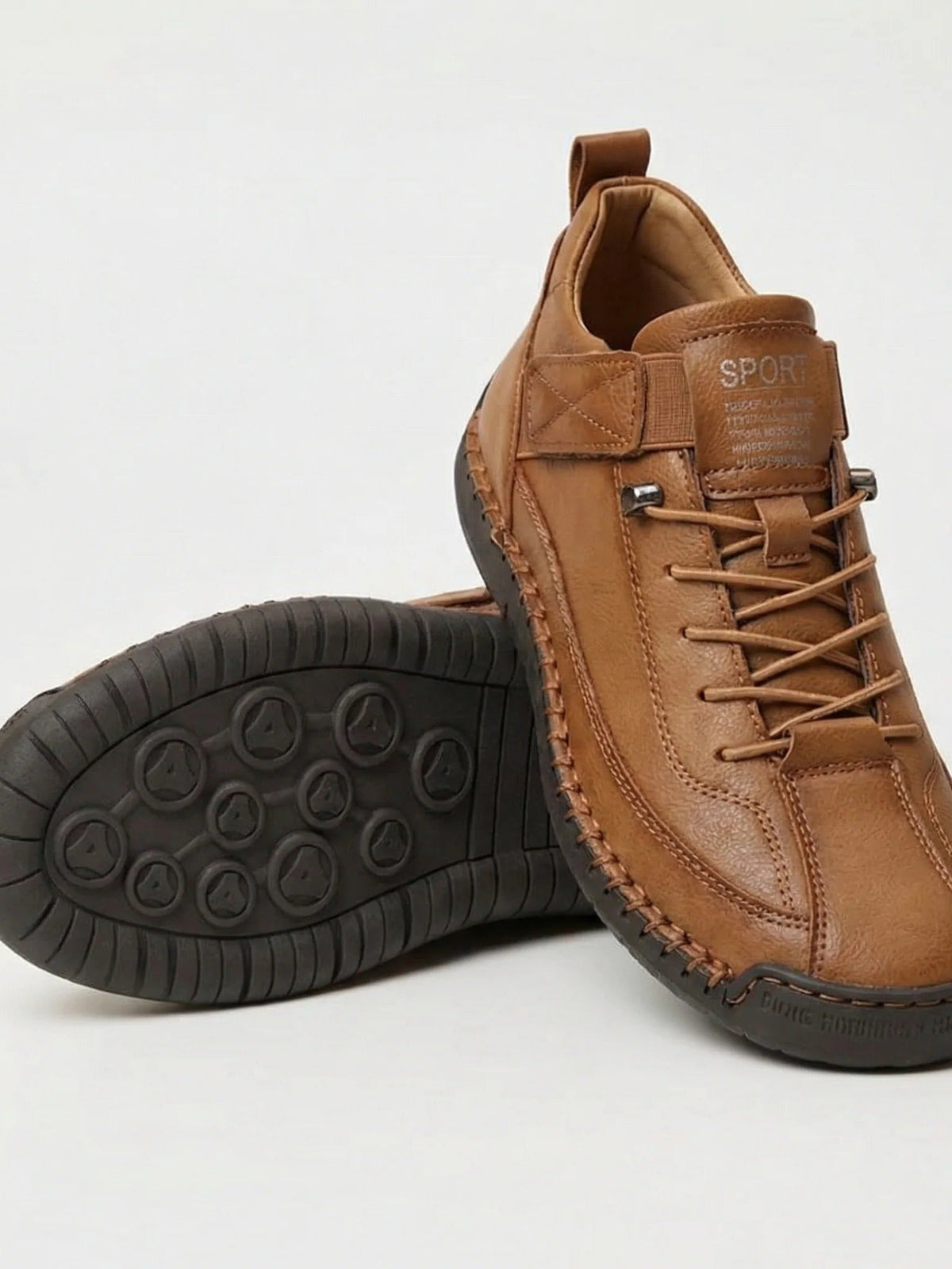 Pair of tan trainers with contrast stitching, one resting on its side to show the dark studded sole 6