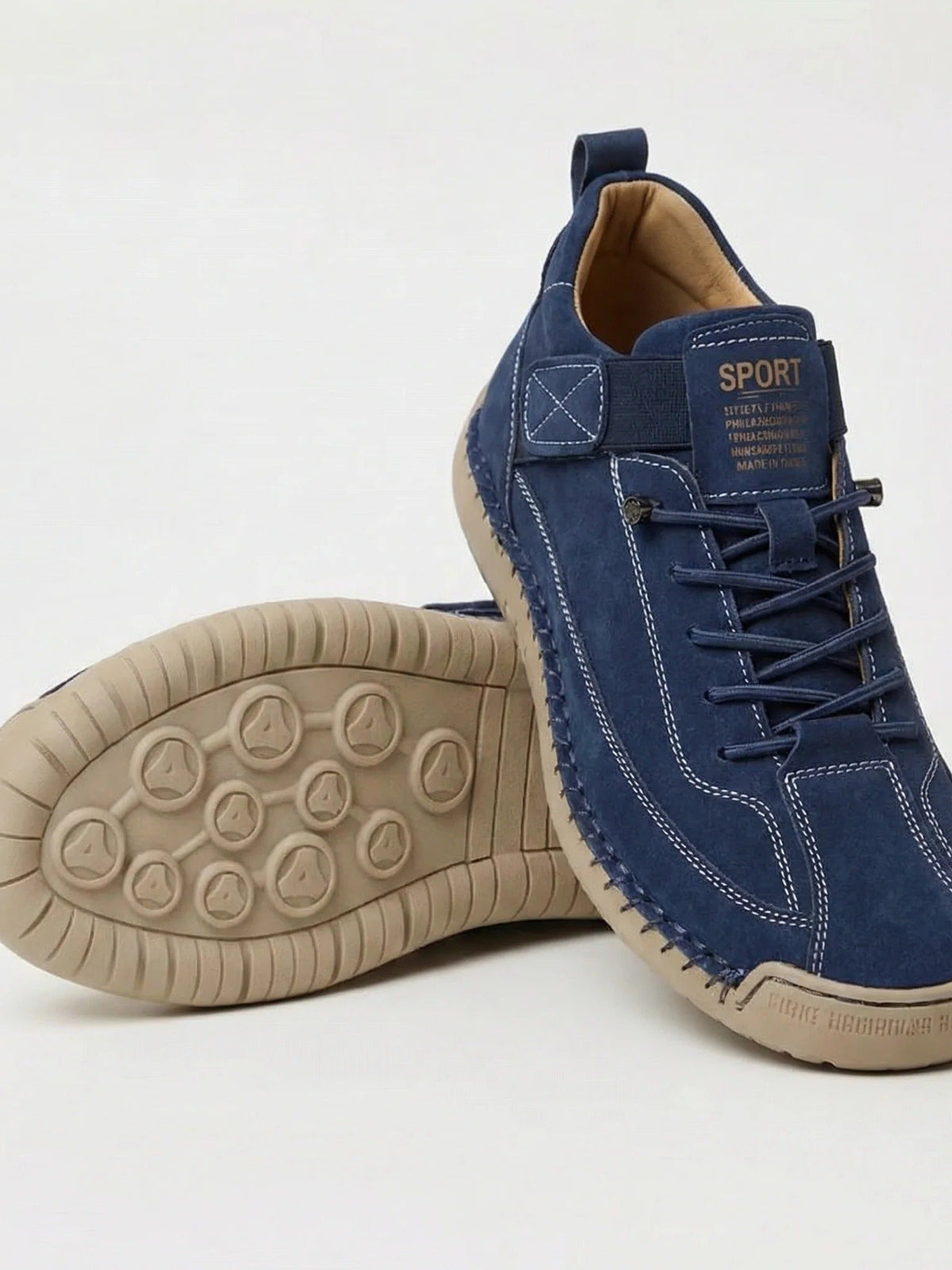 Navy suede-look trainer with white stitching and elastic laces, beside a second shoe showing its tan studded sole 2