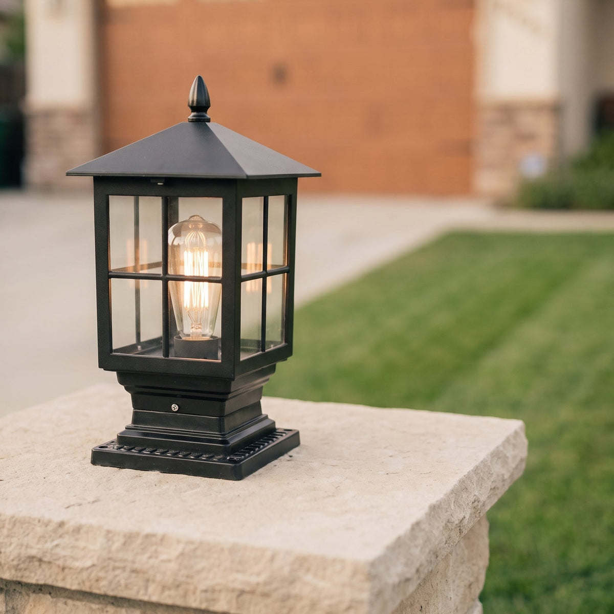 Glowing black post lamp standing on a pale stone pillar, with a lawn and driveway softly blurred behind. 3