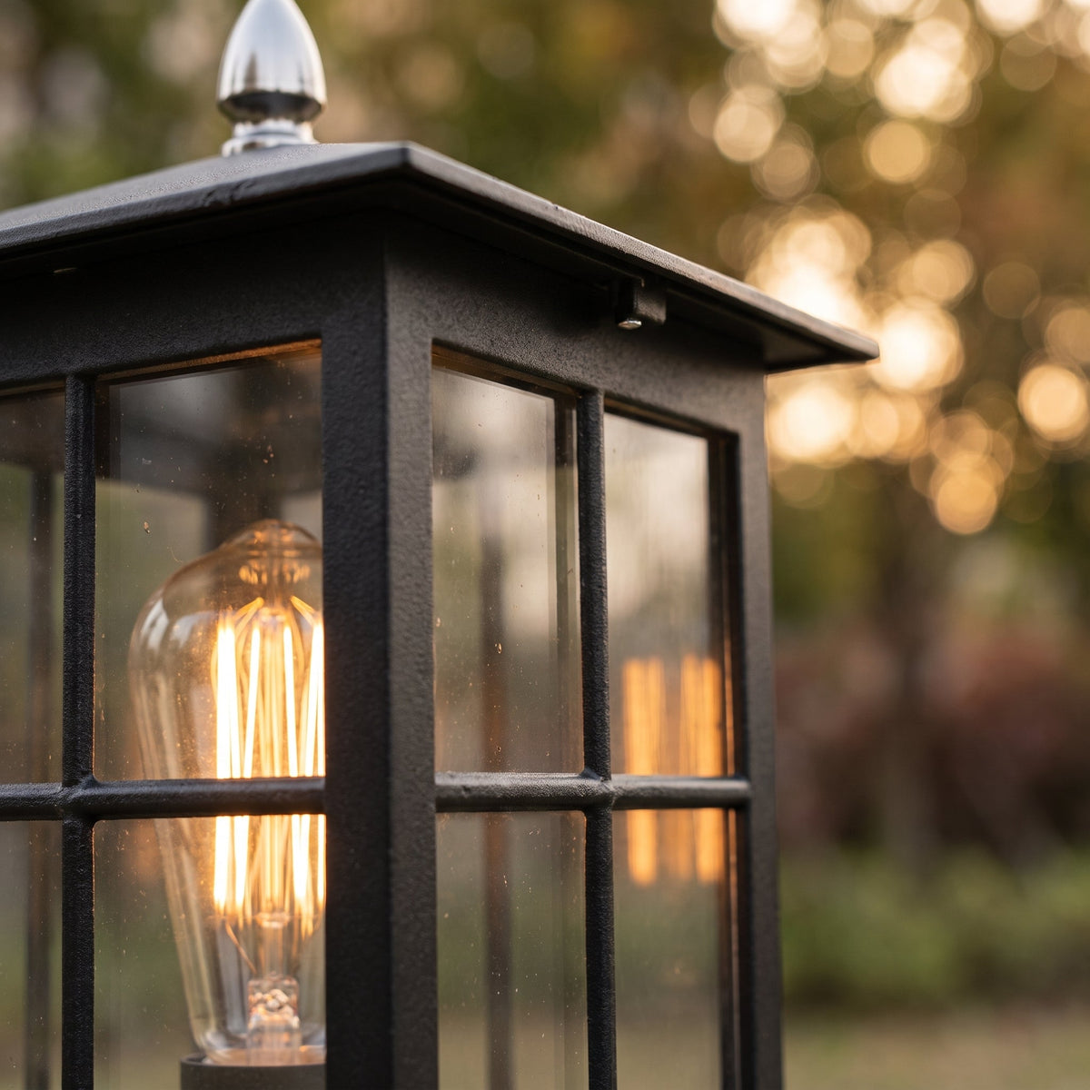 Close-up of the textured black frame, glass panes and glowing filament bulb, with a silver-coloured finial at the top. 5