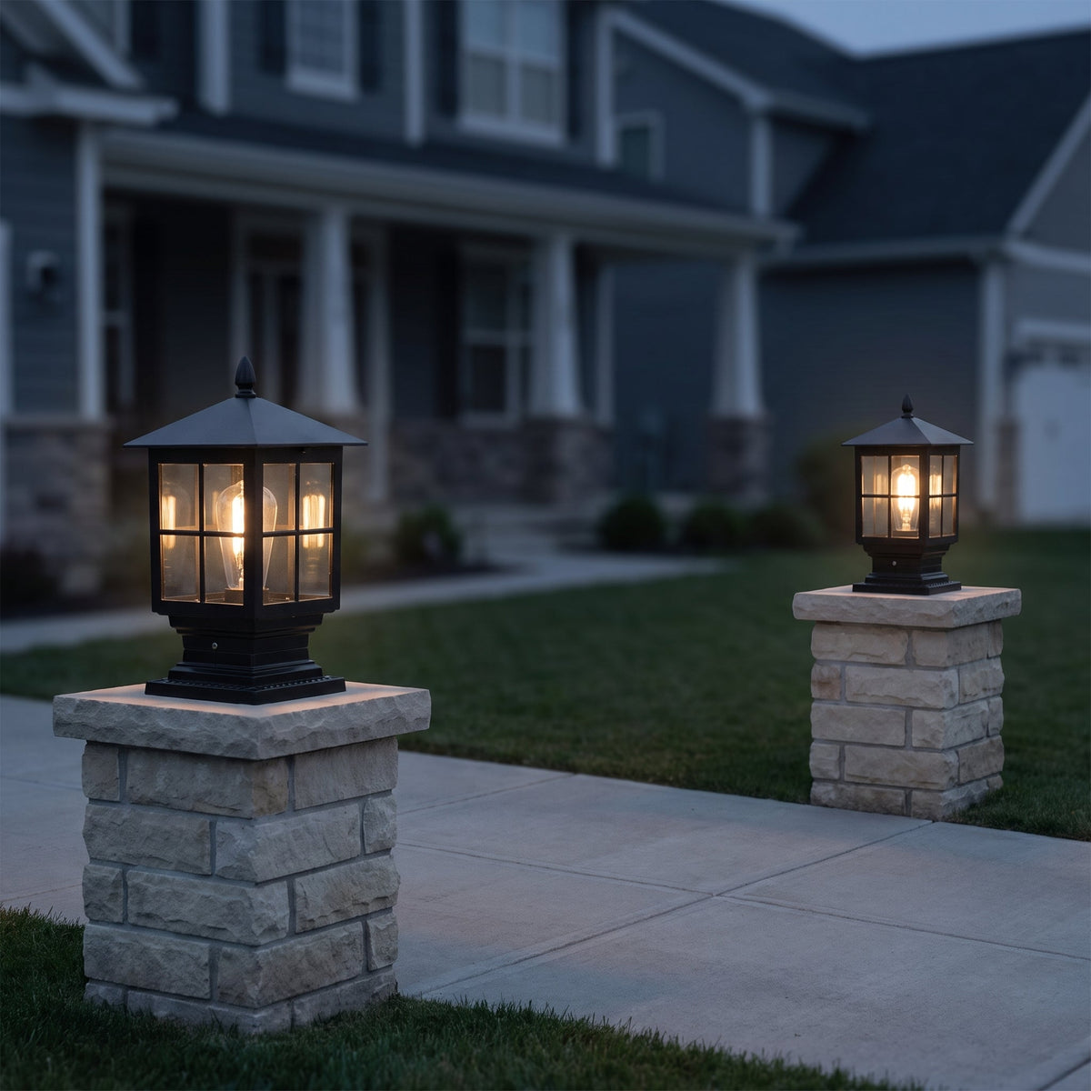 Two lit black pillar lamps on stone gateposts beside a pavement at dusk, with a house in the background. 7