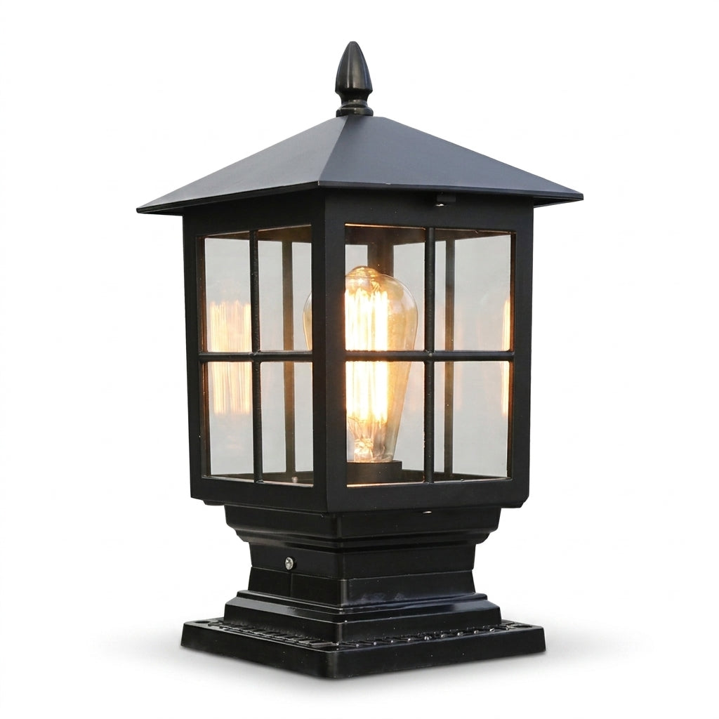Black pillar lamp with a pyramid roof, acorn finial and glass panes, shown on a plain white background with a glowing filament bulb. 1