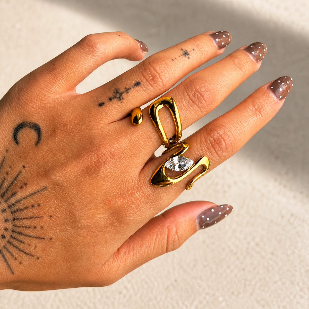 Ring worn on a tattooed hand beside a larger gold ring with a clear marquise-cut stone 4
