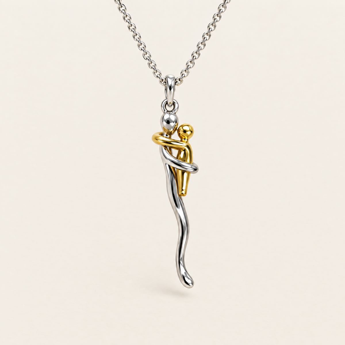 Front view of the silver chain and pendant showing a gold-tone figure embraced by a silver figure, against a plain cream background. 1