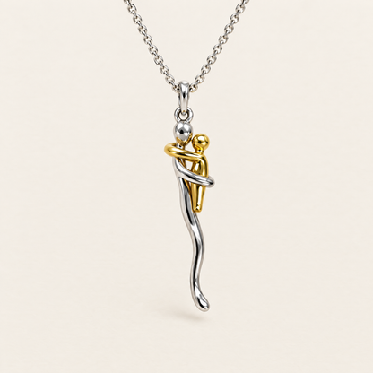 Front view of the silver chain and pendant showing a gold-tone figure embraced by a silver figure, against a plain cream background. 1