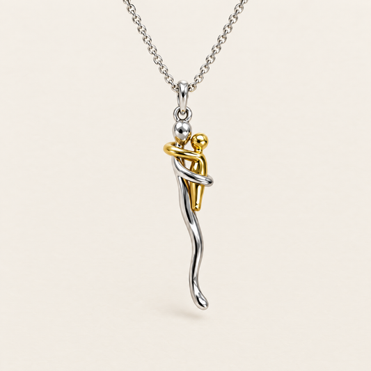 Front view of the silver chain and pendant showing a gold-tone figure embraced by a silver figure, against a plain cream background. 1