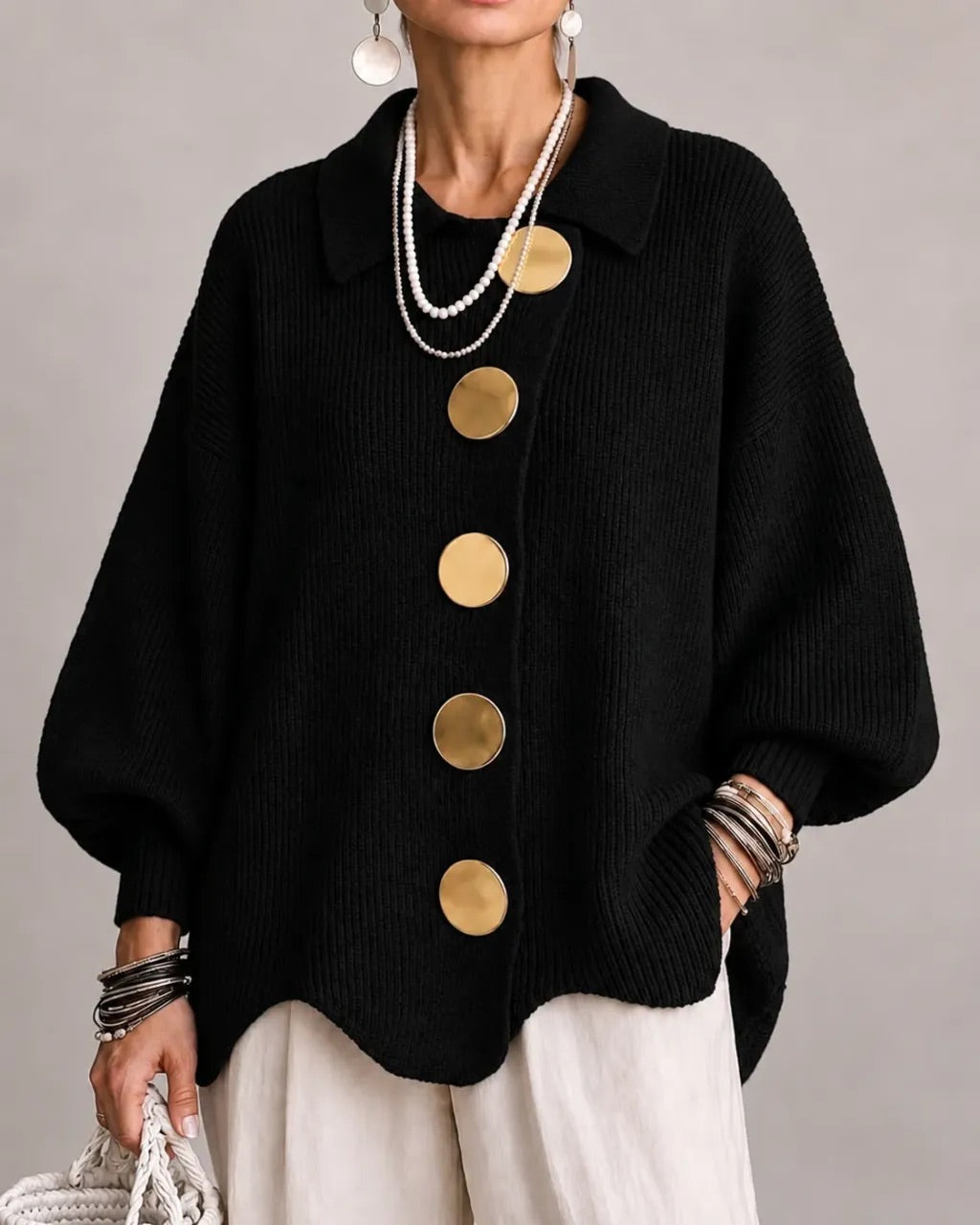 Black ribbed cardigan on a model, with large gold buttons and pointed collar, paired with cream trousers and pearl necklaces. 8