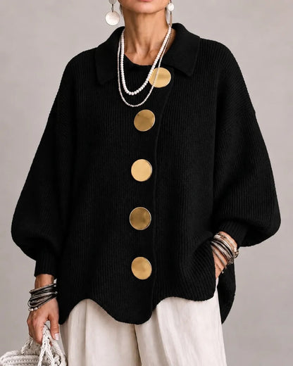 Black ribbed cardigan on a model, with large gold buttons and pointed collar, paired with cream trousers and pearl necklaces. 8