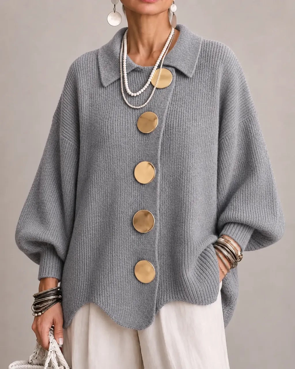 Mid-grey ribbed cardigan on a model, with five oversized gold buttons and balloon sleeves, styled with white trousers. 18