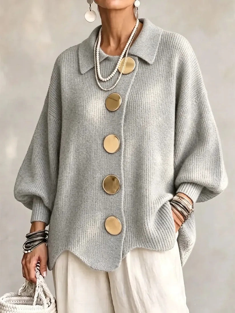 Light grey ribbed cardigan on a model, with gold buttons, pointed collar and scalloped hem, styled with cream trousers. 10