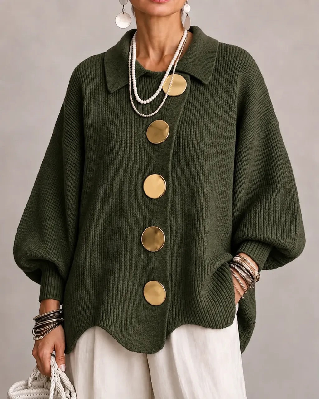 Dark olive-green ribbed cardigan on a model, with large gold buttons and pointed collar, worn with white trousers. 12