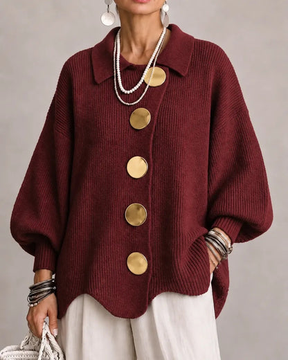 Burgundy ribbed cardigan on a model, with big gold buttons, pointed collar and scalloped hem, worn with white trousers. 19