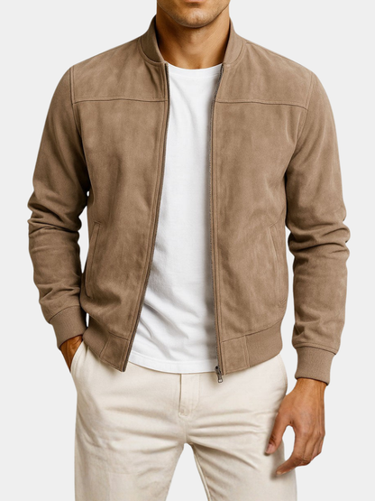 Tan jacket on a plain white background, worn open over a white t-shirt and cream trousers, showing the zip and front pockets. 6
