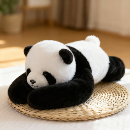Black and white panda plush lying on its tummy on a woven straw mat, long soft arms curled around its head. 1