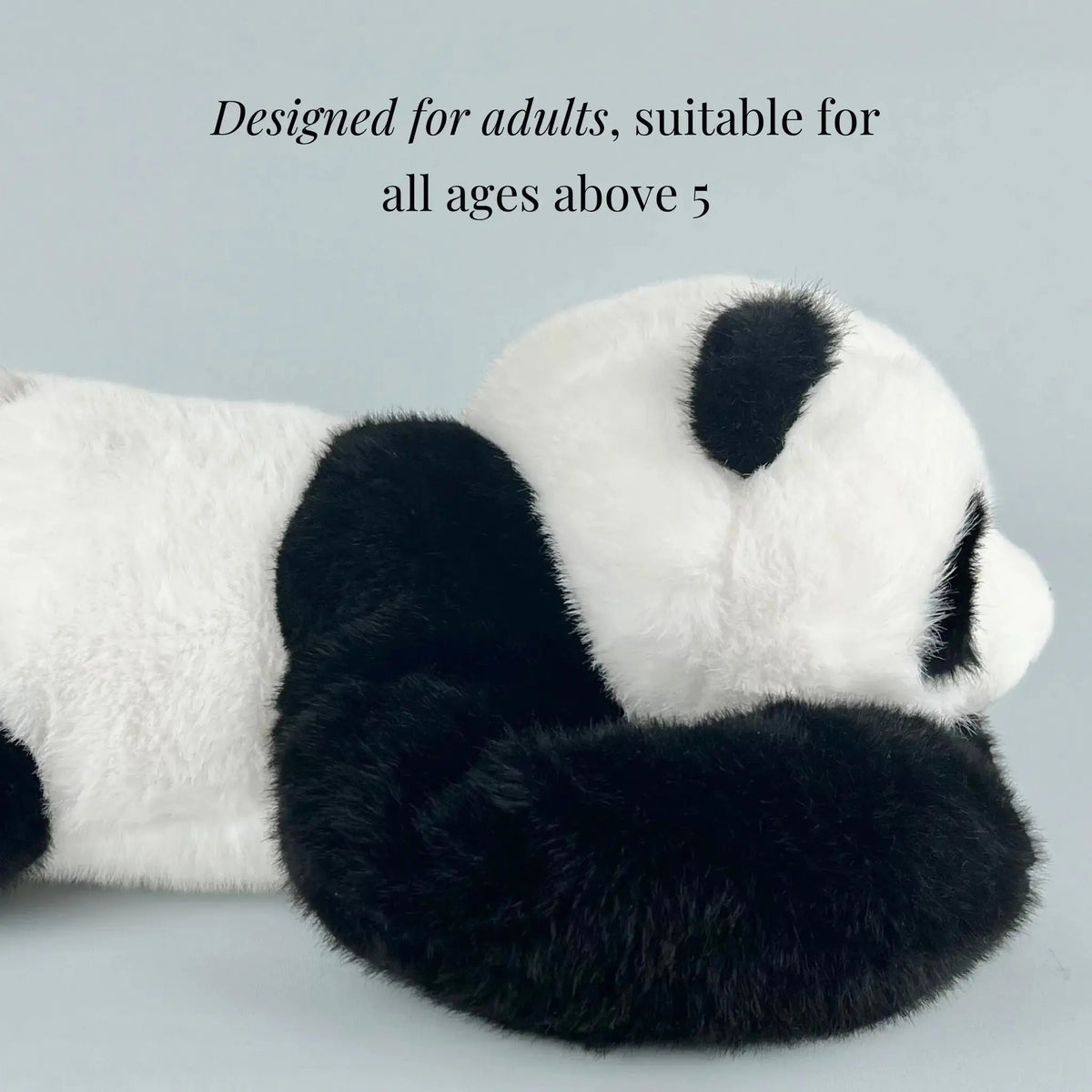 Side view of the panda plush lying flat, showing its fluffy white body, black ear and long black arm stretched forward. 6