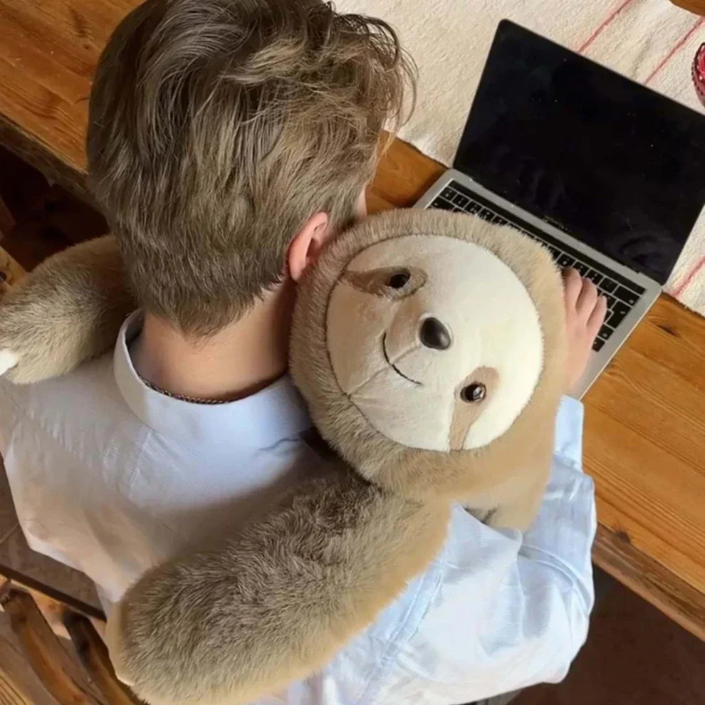 View from above of a man working at a laptop with a sloth plush hugging his neck and shoulders. 9