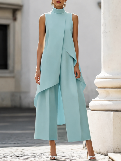 Front view in light blue on a model by a stone column, with the layered asymmetric top over wide trousers. 4