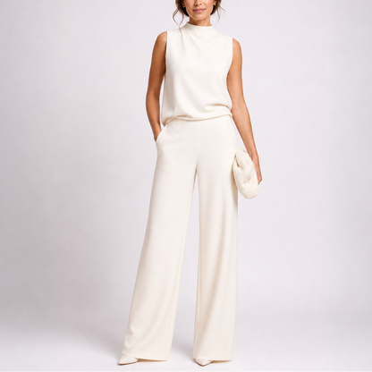 Model wearing the sleeveless jumpsuit in cream with matching pointed shoes and a fluffy clutch 2