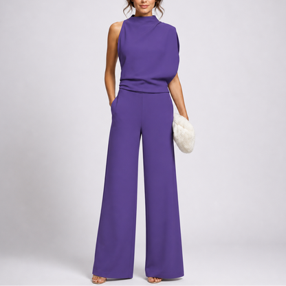 Model wearing the jumpsuit in purple with an asymmetric draped bodice and strappy sandals 3