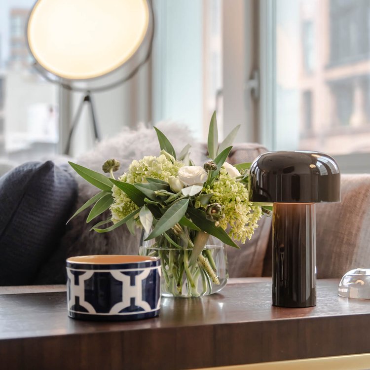 Black glossy mushroom lamp on a wooden side table beside a flower vase and patterned bowl 16