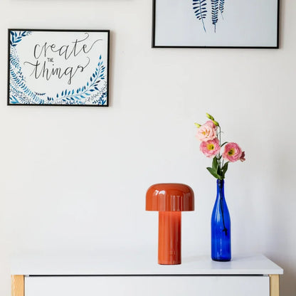 Orange mushroom lamp on a white chest of drawers beside a blue vase of pink flowers 20