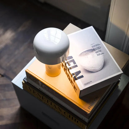 White mushroom-shaped lamp glowing warmly on a stack of art books beside a window 21