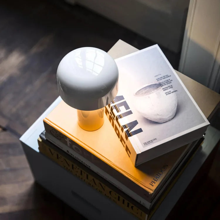 White glossy mushroom lamp glowing warmly on a stack of large coffee-table books 21
