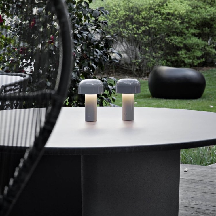 Pair of grey mushroom lamps lit on a round outdoor table with a garden behind 23