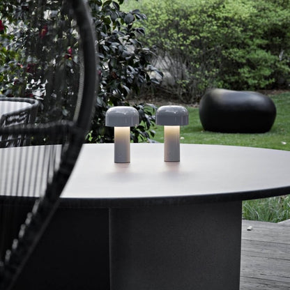 Pair of grey lamps lit on a round outdoor table, with garden and shrubs behind 23