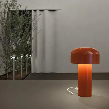 Glossy orange-red lamp lit on a surface, with a white charging cable plugged into its base 25