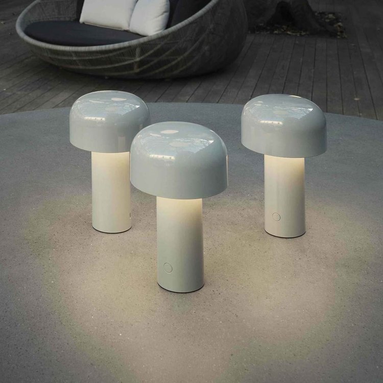 Three pale grey lamps glowing on a round outdoor table, with a woven garden chair behind 7
