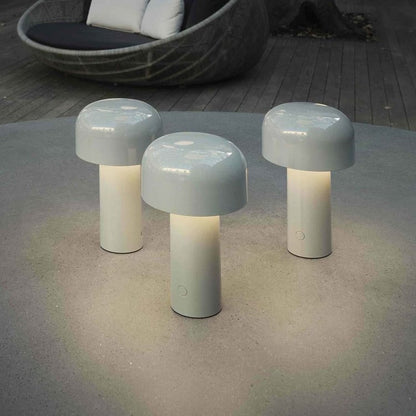 Three pale grey mushroom lamps lit outdoors on a round concrete table, a wicker seat behind 7