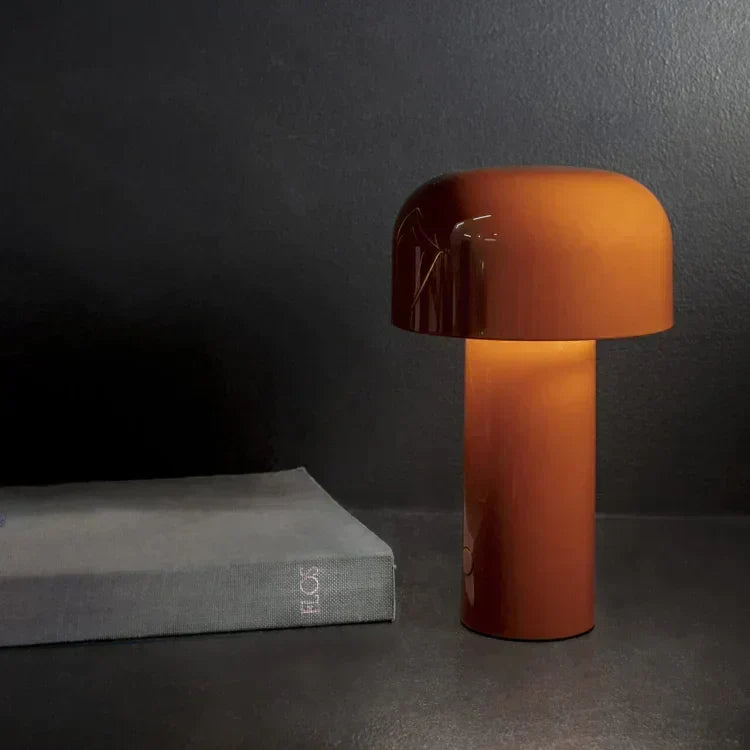 Glossy orange mushroom lamp glowing warmly against a dark wall, next to a grey book 8