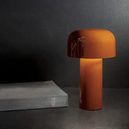 Burnt-orange lamp lit against a dark wall, standing beside a grey hardback book 8