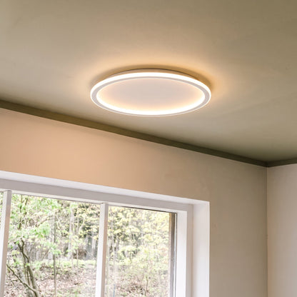 Glowing white ring light on a ceiling above a white-framed window overlooking green trees. 8