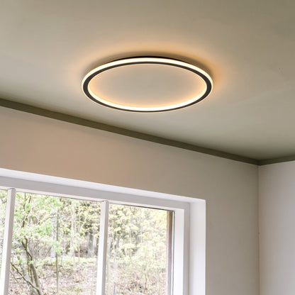 Lit ring ceiling light in a room corner, with a white-framed window showing trees outside. 8