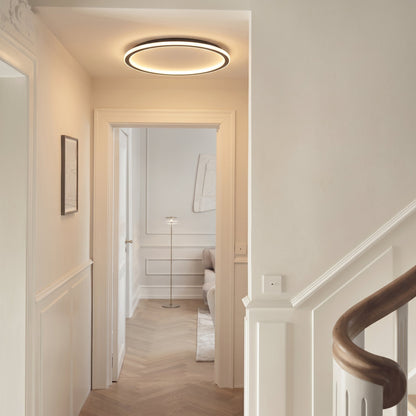 Lit ring light fitted in a hallway ceiling, with panelled walls, a staircase handrail and a doorway to another room. 5