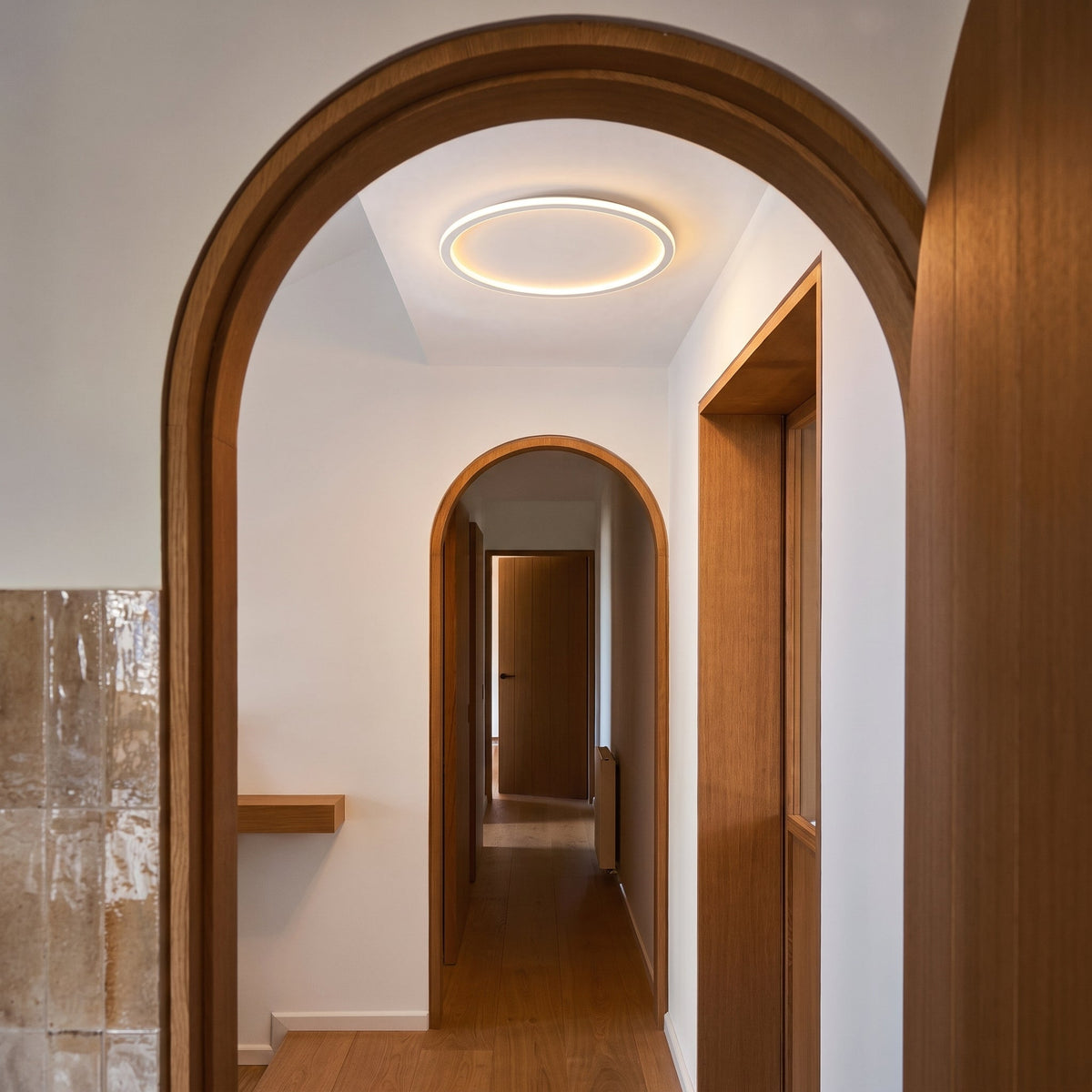 Glowing ring light on the ceiling of a narrow hallway, seen through a wooden arched doorway with oak doors and floor. 4
