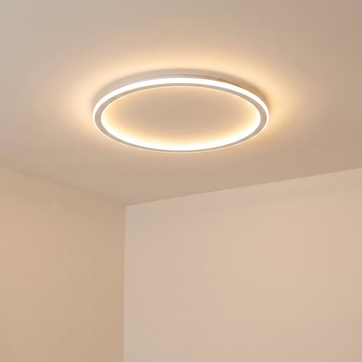 Angled view of the lit ring light on a cream ceiling beside a corner, showing its slim profile and soft warm glow. 6